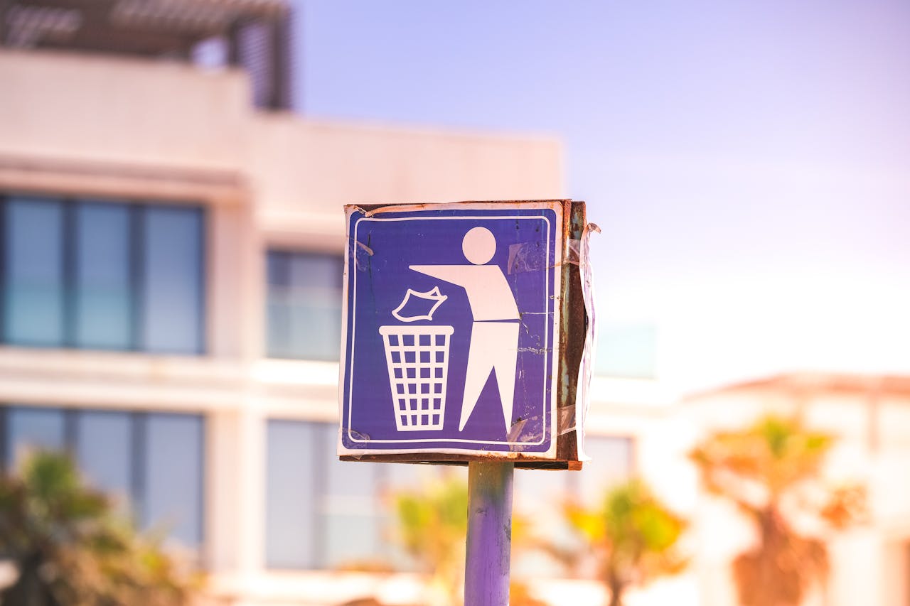 Close-up of a recycling sign against a modern building backdrop in a sunny urban setting.